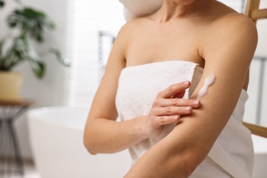 Woman applying self-tanning product onto arm in bathroom, closeup. Space for text