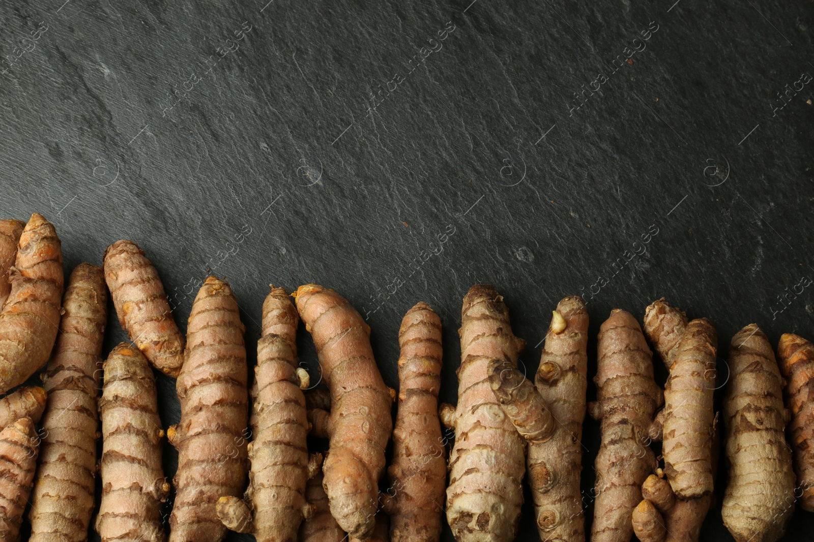 Photo of Many raw turmeric roots on black textured table, flat lay. Space for text