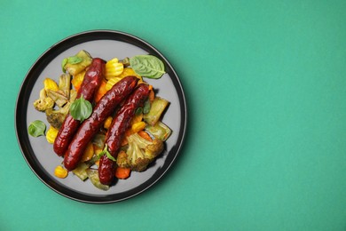 Photo of Delicious smoked sausage and baked vegetables on green background, top view. Space for text