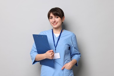 Photo of Portrait of smiling medical assistant with clipboard on grey background