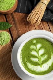 Delicious matcha latte, powder, leaf and whisk on wooden table, flat lay