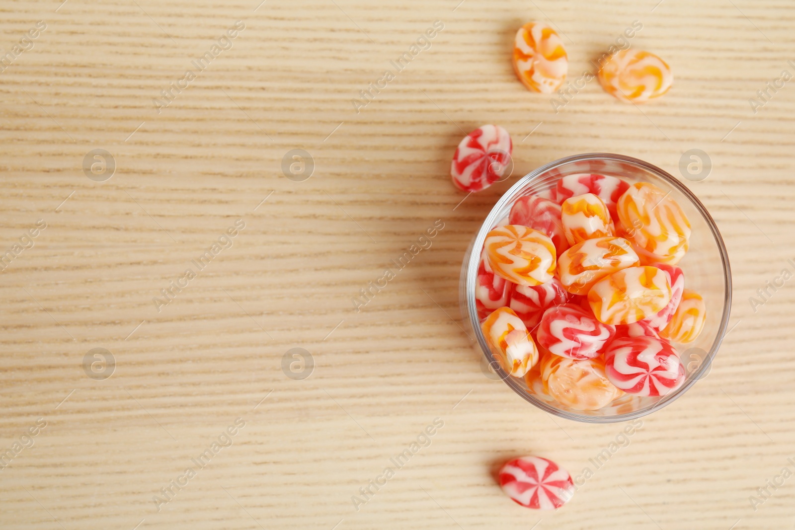 Photo of Flat lay composition with glass of delicious colorful candies and space for text on wooden background