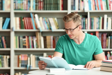 Young man reading book at table in library. Space for text