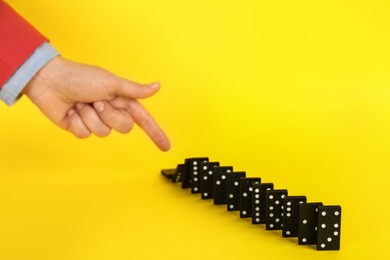 Photo of Woman causing chain reaction by pushing domino tile on yellow background, closeup