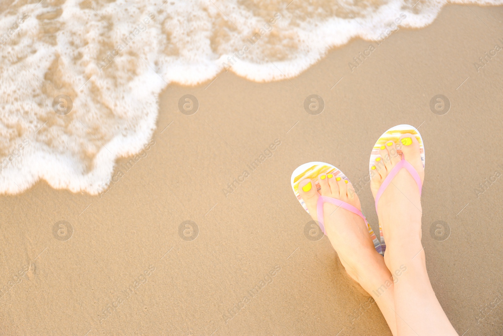 Photo of Closeup of woman with stylish flip flops on sand near sea, space for text. Beach accessories