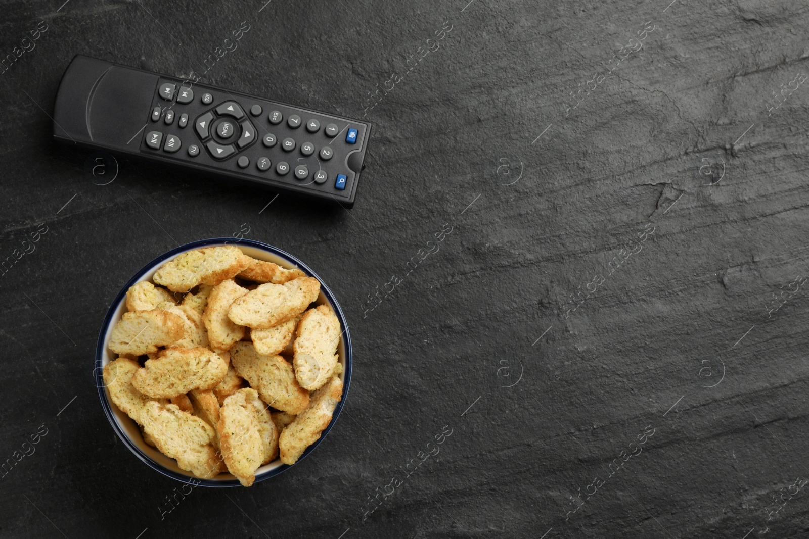 Photo of Modern tv remote control and rusks on black table, flat lay. Space for text