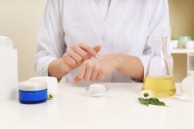 Female dermatologist testing skin care product at table, closeup