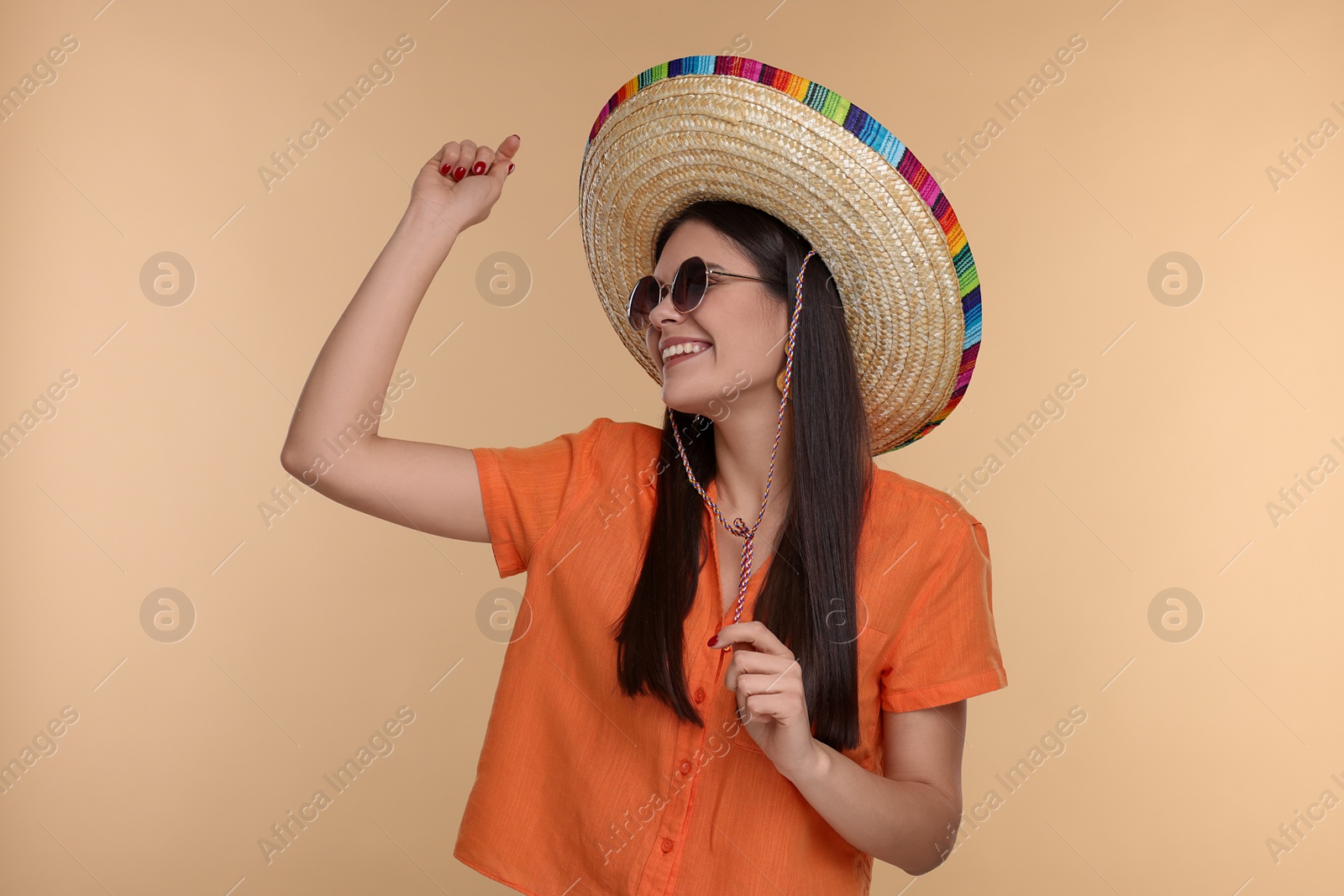 Photo of Young woman in Mexican sombrero hat and sunglasses dancing on beige background