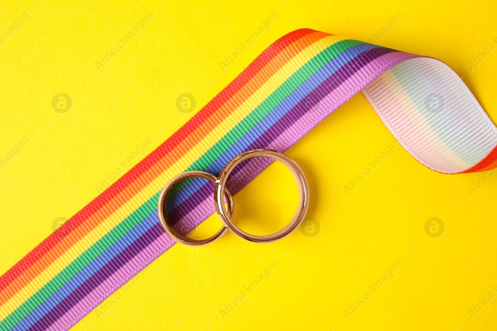 Photo of Wedding rings and rainbow ribbon on color background, top view. Gay symbol