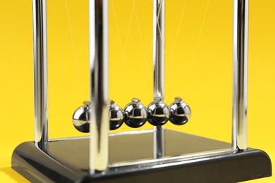 Photo of Newton's cradle on yellow background, closeup. Physics law of energy conservation