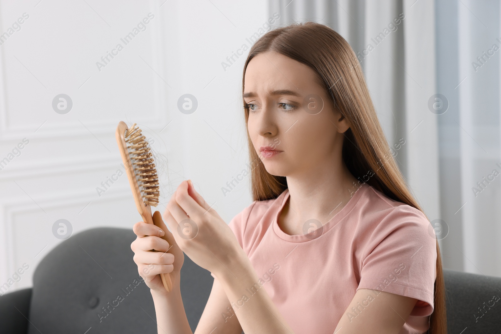 Photo of Emotional woman untangling her lost hair from brush at home. Alopecia problem