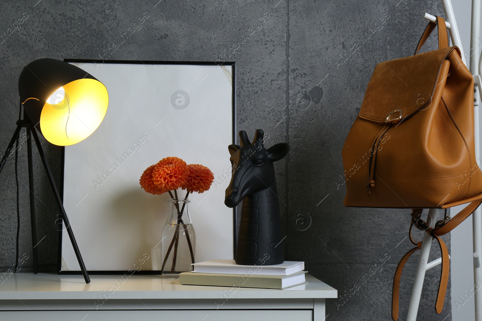 Photo of Stylish decor, vase with flowers, picture and desk lamp on white table near grey wall in hallway. Interior design