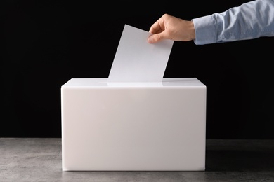 Photo of Man putting his vote into ballot box on table against black background, closeup