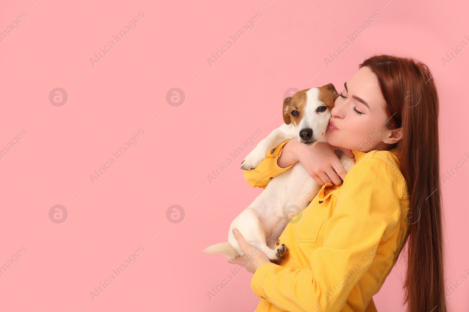 Photo of Woman kissing her cute Jack Russell Terrier dog on pink background. Space for text