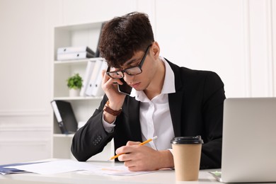 Photo of Young man talking on phone while working at table in office. Deadline concept