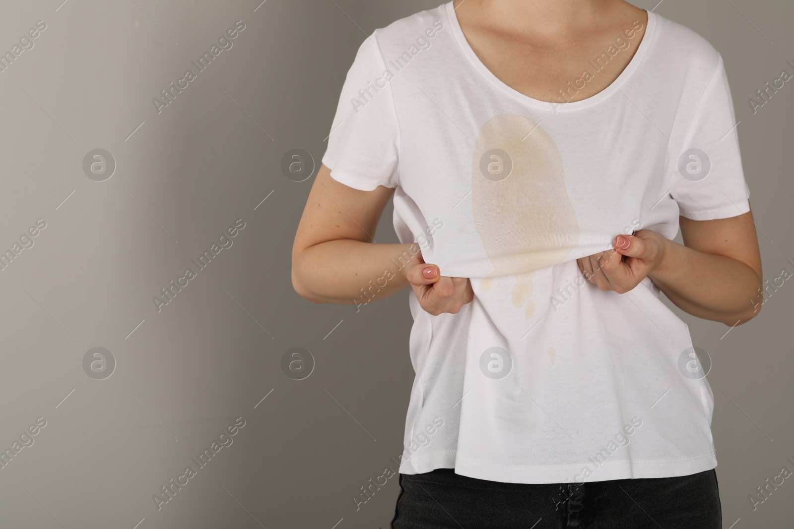 Photo of Woman showing stain from coffee on her shirt against light grey background, closeup. Space for text