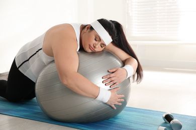 Lazy overweight woman leaning on fit ball instead of training at gym