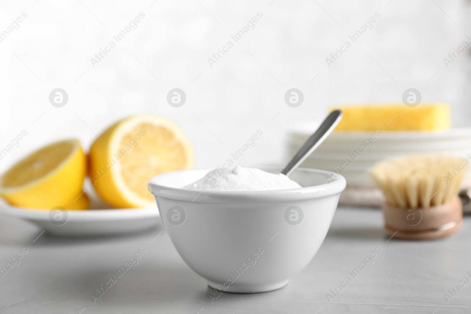 Photo of Bowl of baking soda, brush and lemon on light grey table