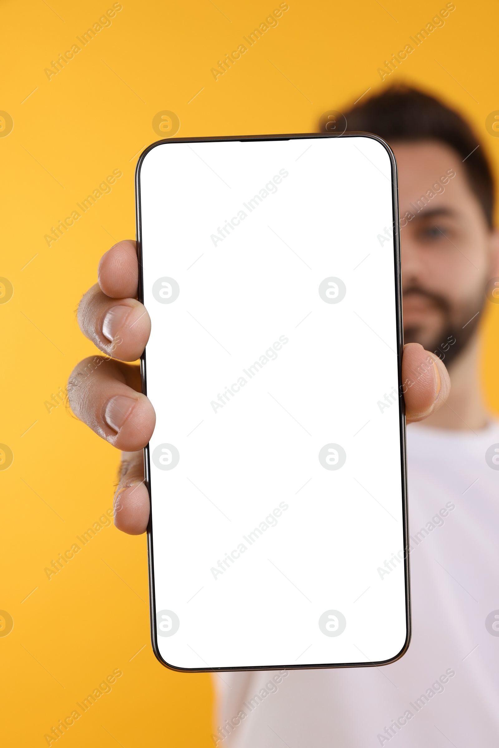 Photo of Man holding smartphone with blank screen on yellow background, selective focus