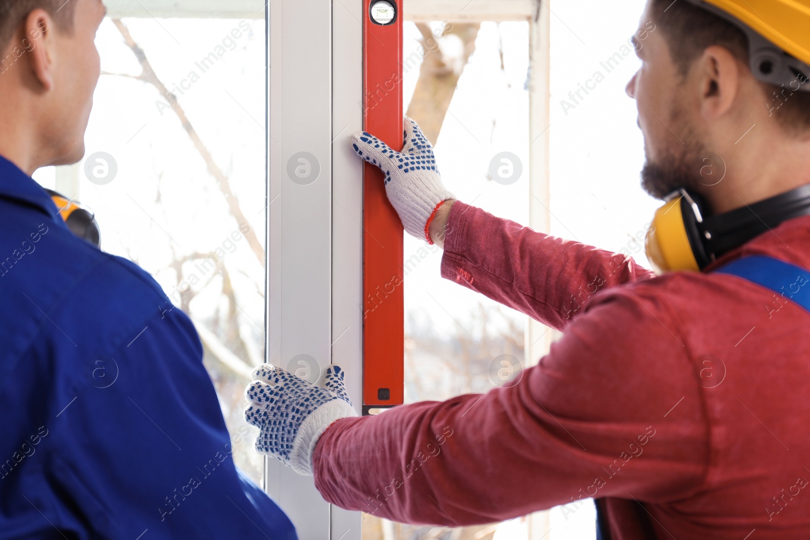 Photo of Workers using bubble level for installing window indoors, closeup