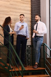 Photo of Group of coworkers talking during coffee break on stairs in office