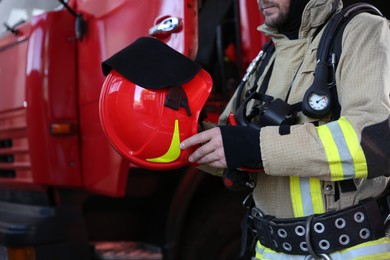 Firefighter in uniform with helmet near red fire truck at station, closeup