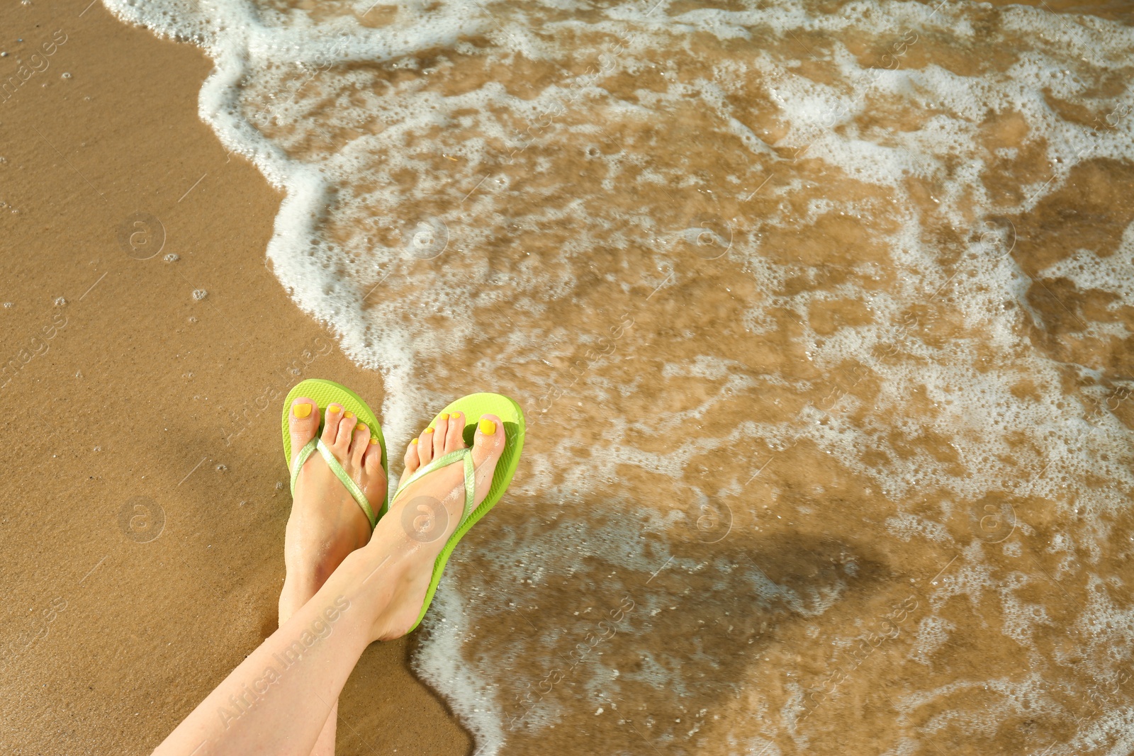 Photo of Closeup of woman with flip flops on sand near sea, space for text. Beach accessories