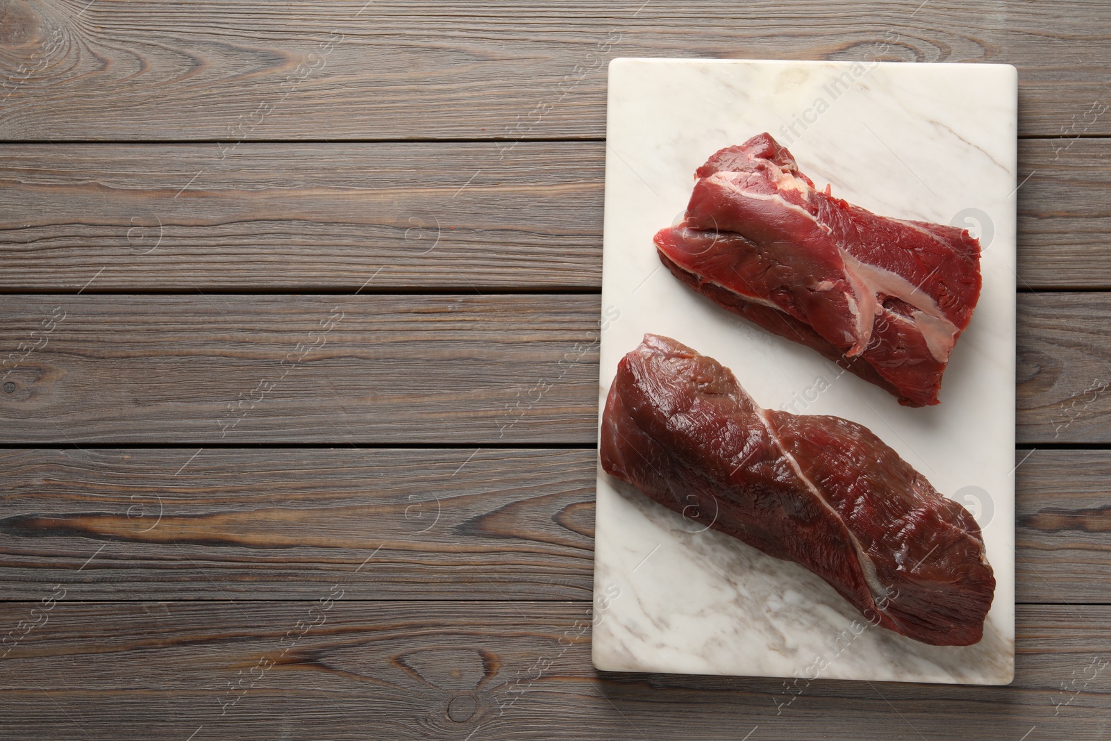 Photo of Pieces of raw beef meat on wooden table, top view. Space for text