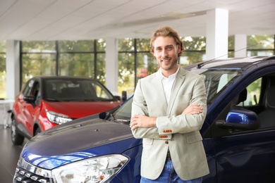 Young man near new car in modern auto dealership