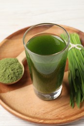 Photo of Wheat grass drink in shot glass, spoon of green powder and fresh sprouts on white table, closeup