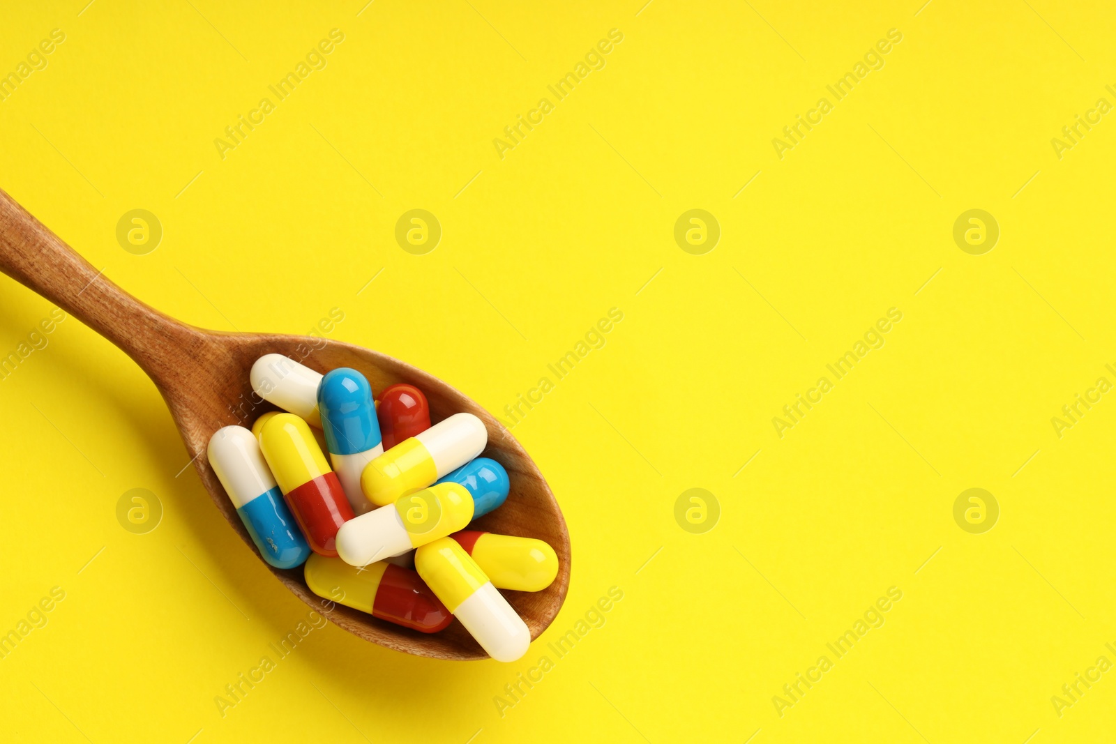 Photo of Antibiotic pills and spoon on yellow background, top view. Space for text