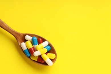 Antibiotic pills and spoon on yellow background, top view. Space for text