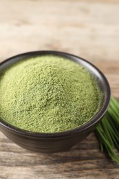 Photo of Wheat grass powder in bowl on wooden table, closeup