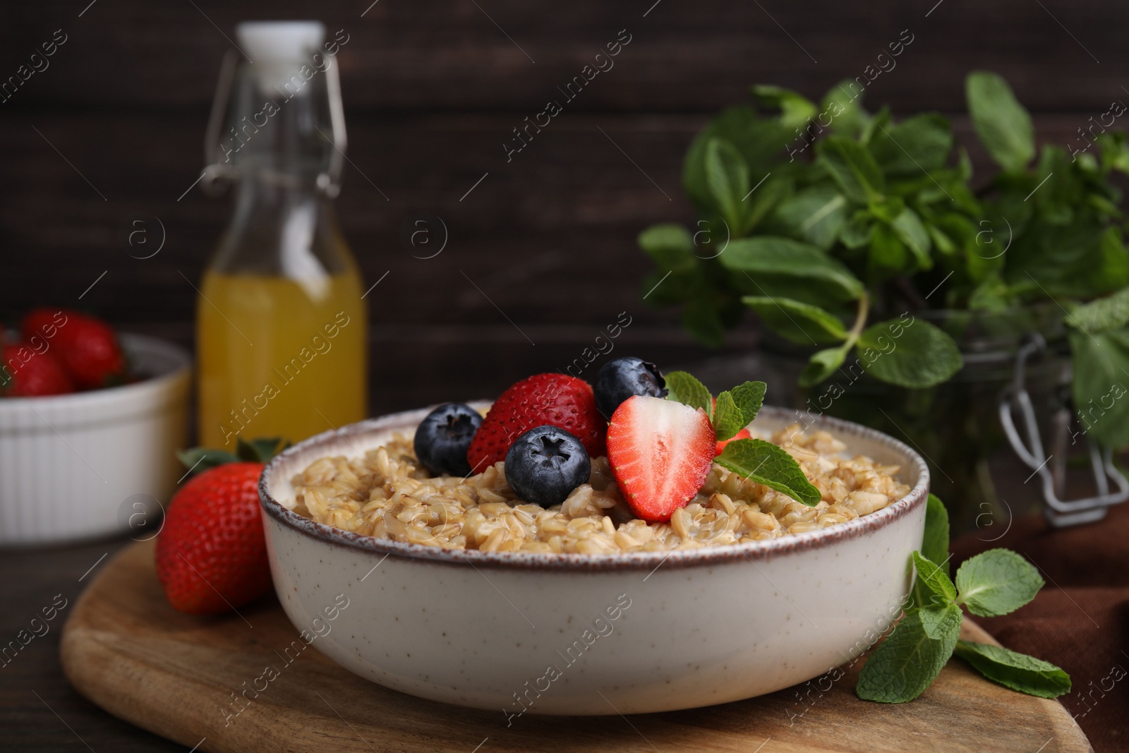 Photo of Tasty oatmeal with strawberries and blueberries in bowl on wooden table