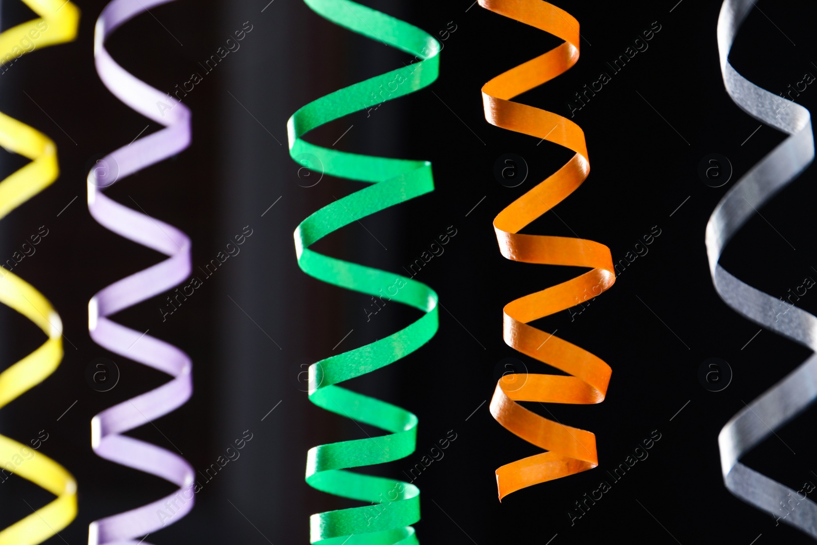 Photo of Many colorful serpentine streamers on black background