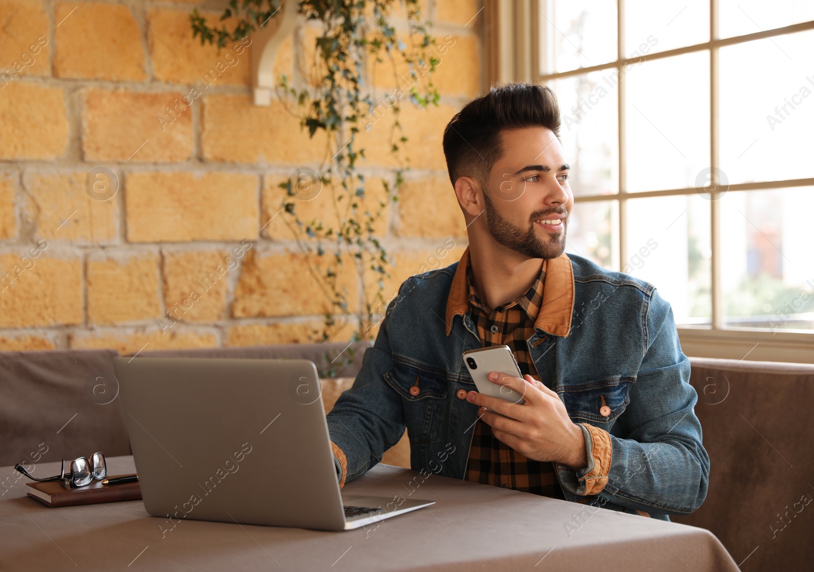 Photo of Young blogger with laptop and phone at table in cafe