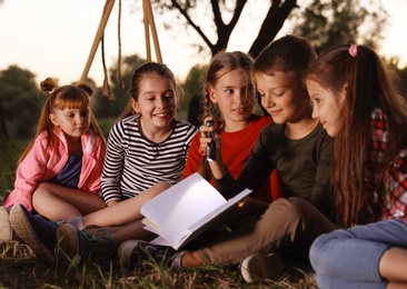 Little children reading book with flashlight outdoors. Summer camp
