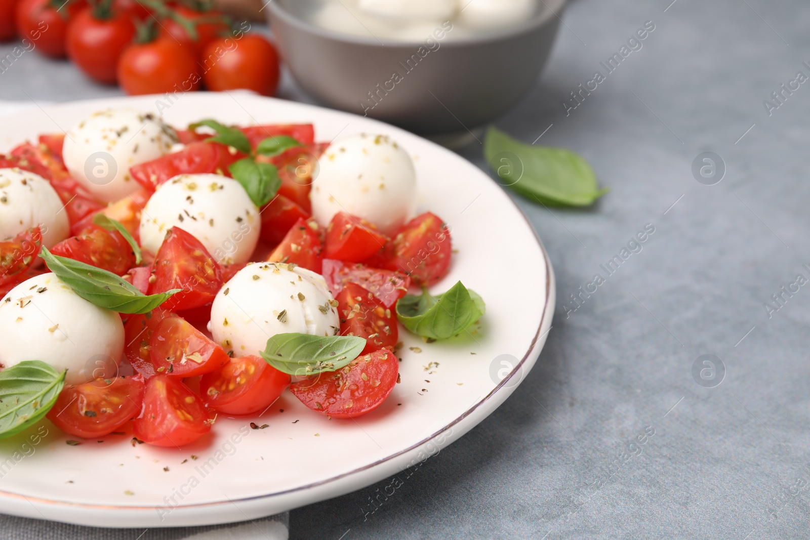 Photo of Tasty salad Caprese with tomatoes, mozzarella balls and basil on grey table, closeup. Space for text