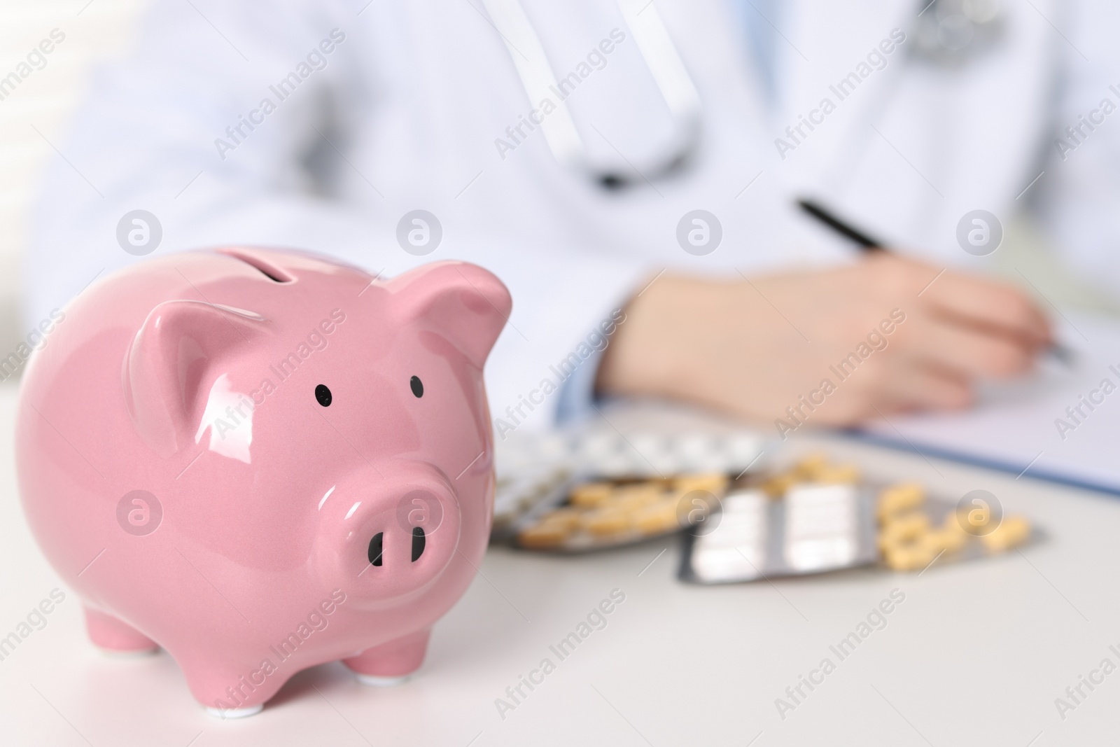 Photo of Doctor making notes at white table, focus on piggy bank