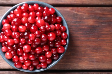 Photo of Fresh ripe cranberries in bowl on wooden table, top view