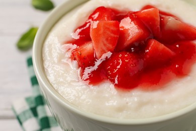 Photo of Delicious semolina pudding with strawberries and jam in bowl on table, closeup