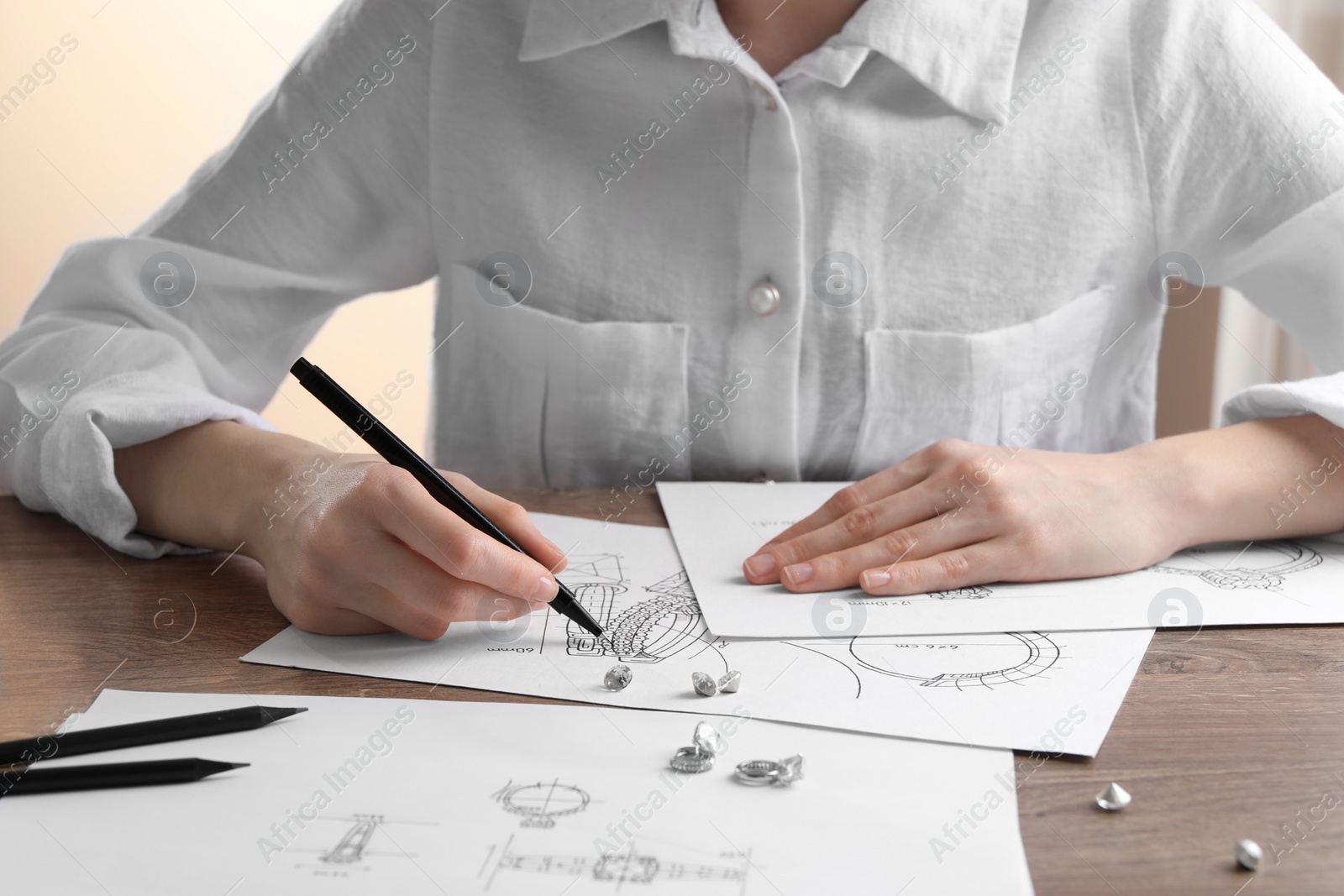 Photo of Jeweler drawing sketch of elegant earrings at wooden table, closeup