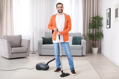 Photo of Young man cleaning carpet with vacuum at home