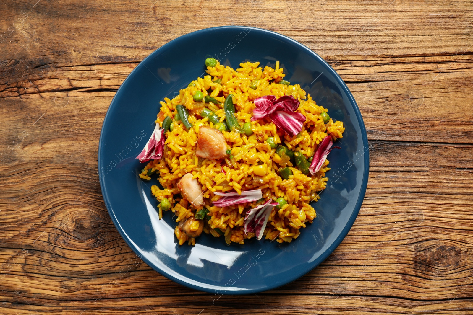 Photo of Delicious rice pilaf with chicken and vegetables on wooden table, top view