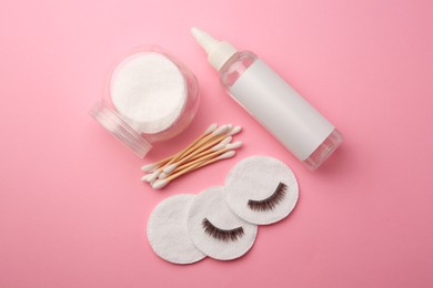 Bottle of makeup remover, false eyelashes, cotton pads and swabs on pink background, flat lay