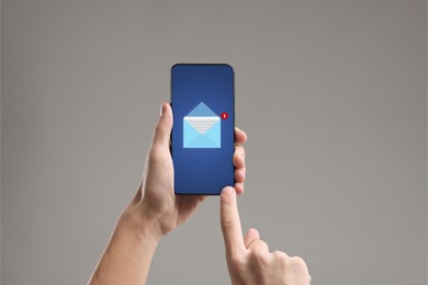 Man checking new message on mobile phone against grey background, closeup