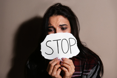 Abused young woman with sign STOP near beige wall. Domestic violence concept