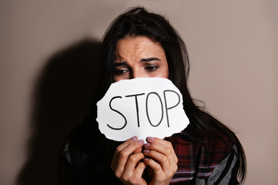 Photo of Abused young woman with sign STOP near beige wall. Domestic violence concept