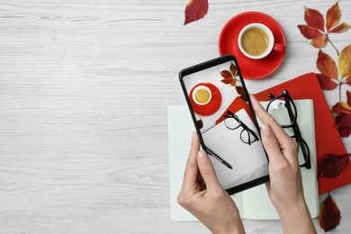 Photo of Woman taking photo of autumn composition with smartphone at white wooden table, top view. Space for text