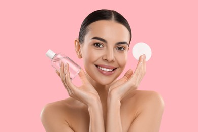 Photo of Beautiful woman holding makeup remover and cotton pad on pink background